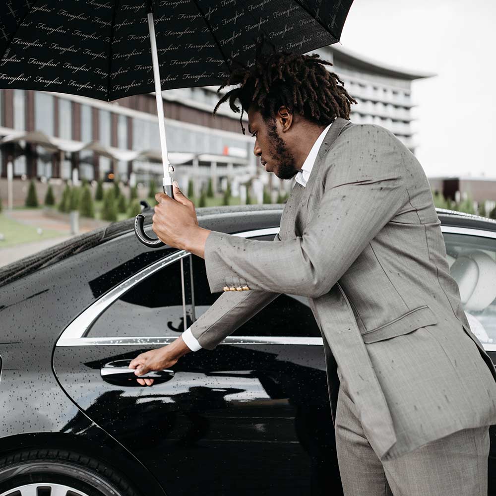 A Mimshack chauffeur holding an umbrella while opening a car door